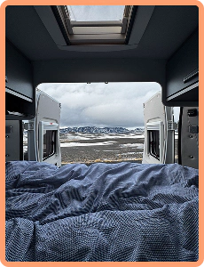 Cozy campervan interior with bed and view of snowy Icelandic mountains through open rear doors